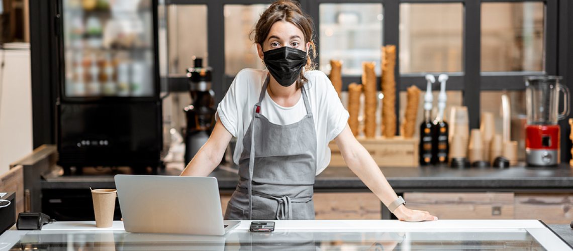 Portrait of a saleswoman or small business owner wearing medical mask at the counter in cafe or small shop. Concept of a retail business during a pandemic